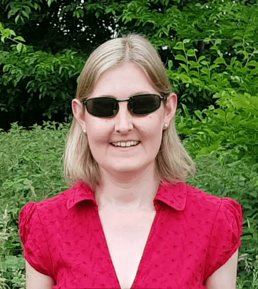 Sally has short blond hair and is wearing dark glasses and a red dress.